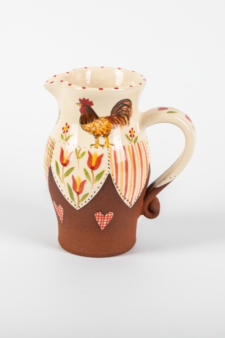 A photo of a decorative ceramic jug with two-tone/patchwork design with a chicken on the side
